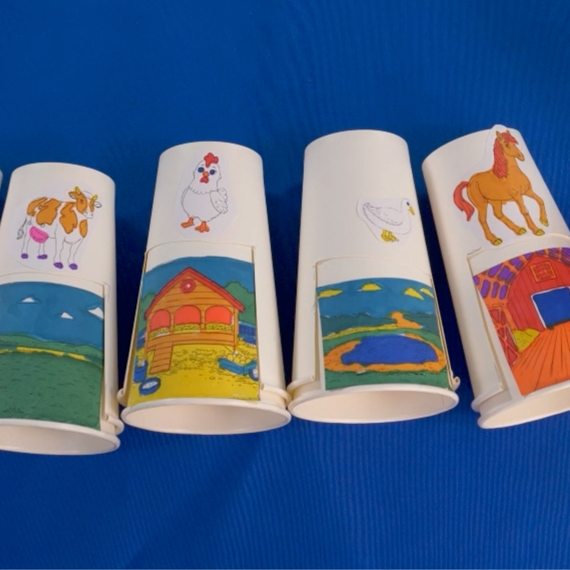 Colorful paper cups with farm animal illustrations on a blue background