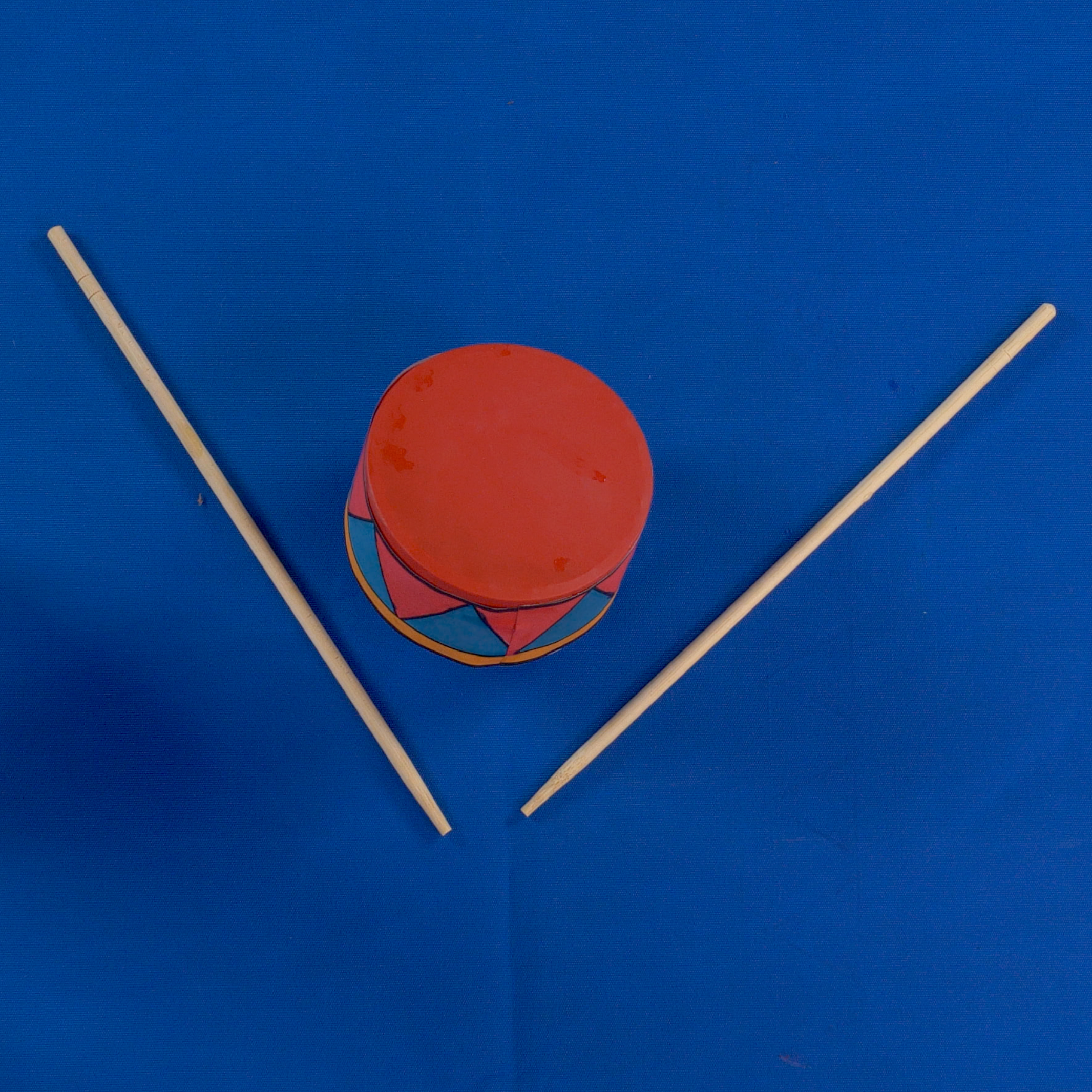Red toy drum with two sticks on a blue background